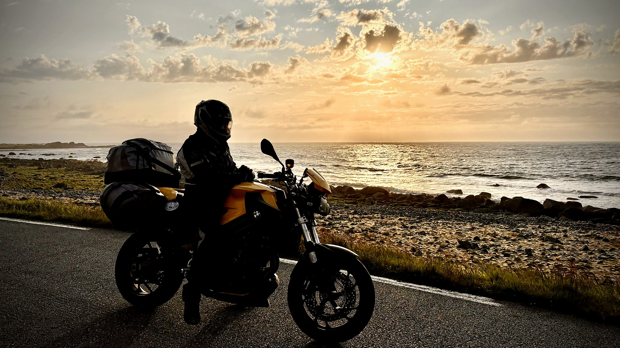 A loaded motorcycle on a coastal road under the midnight sun in Lofoten