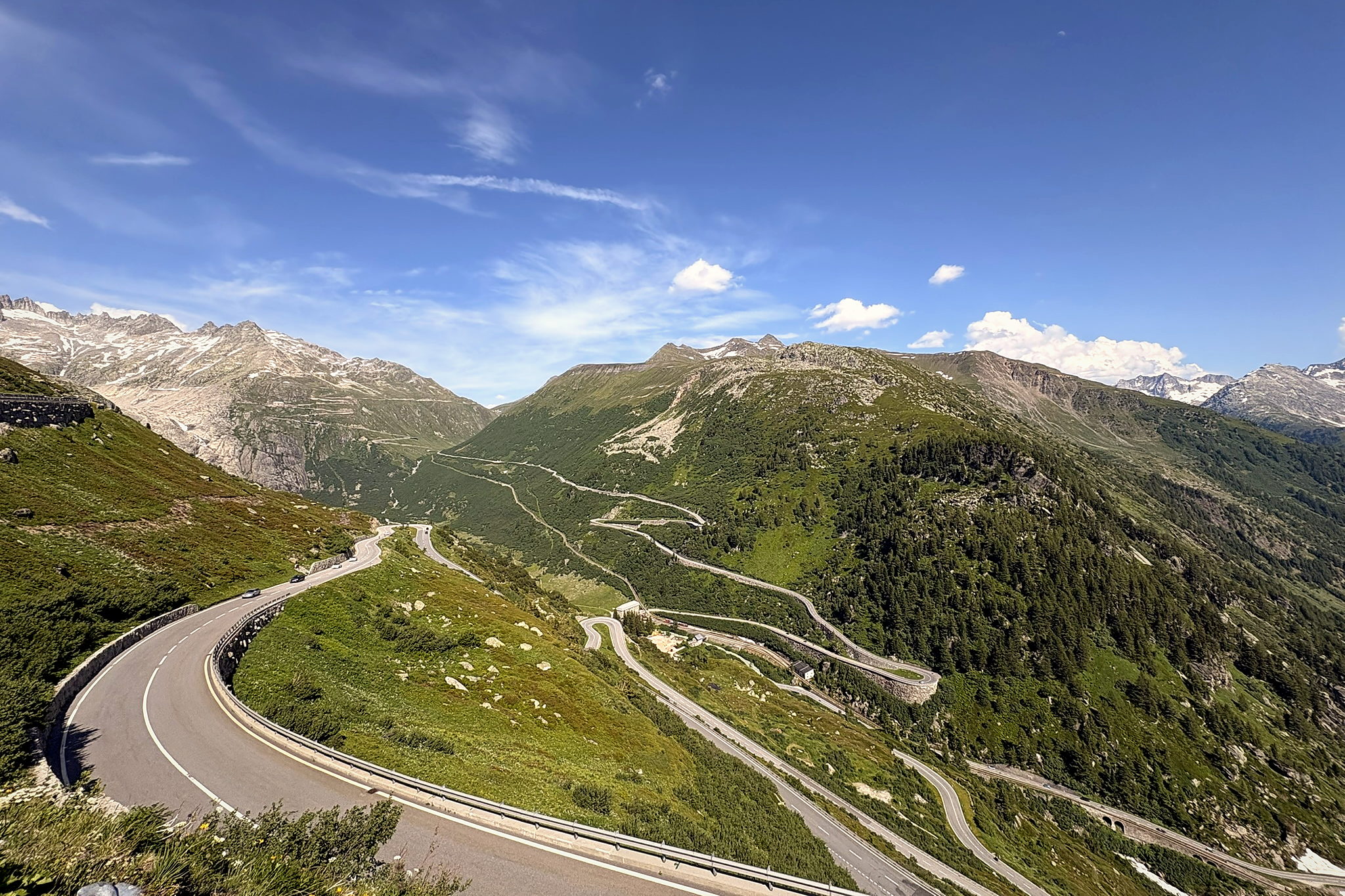 The Grimsel Pass road stacked in hairpins across a green mountainside, snow still on the peaks behind