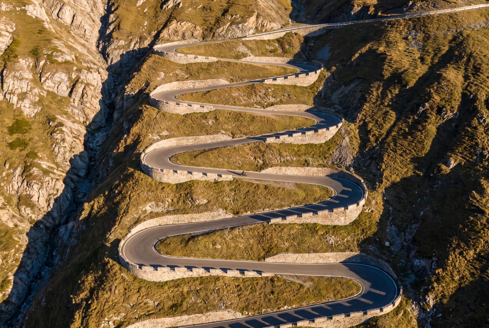 Aerial view of stacked hairpin bends on an alpine pass in golden evening light