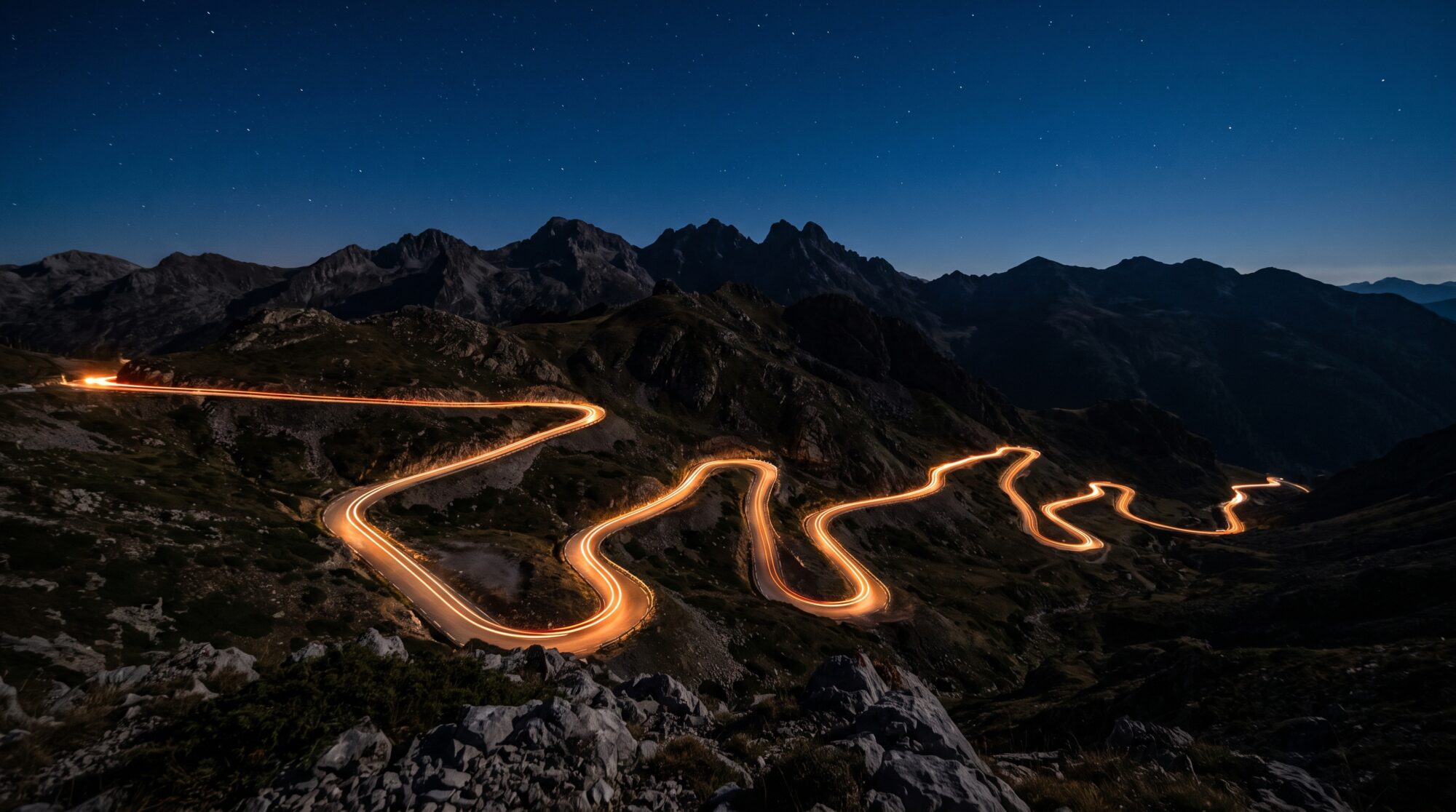 Long-exposure light trail of a motorcycle tracing a winding mountain road at night